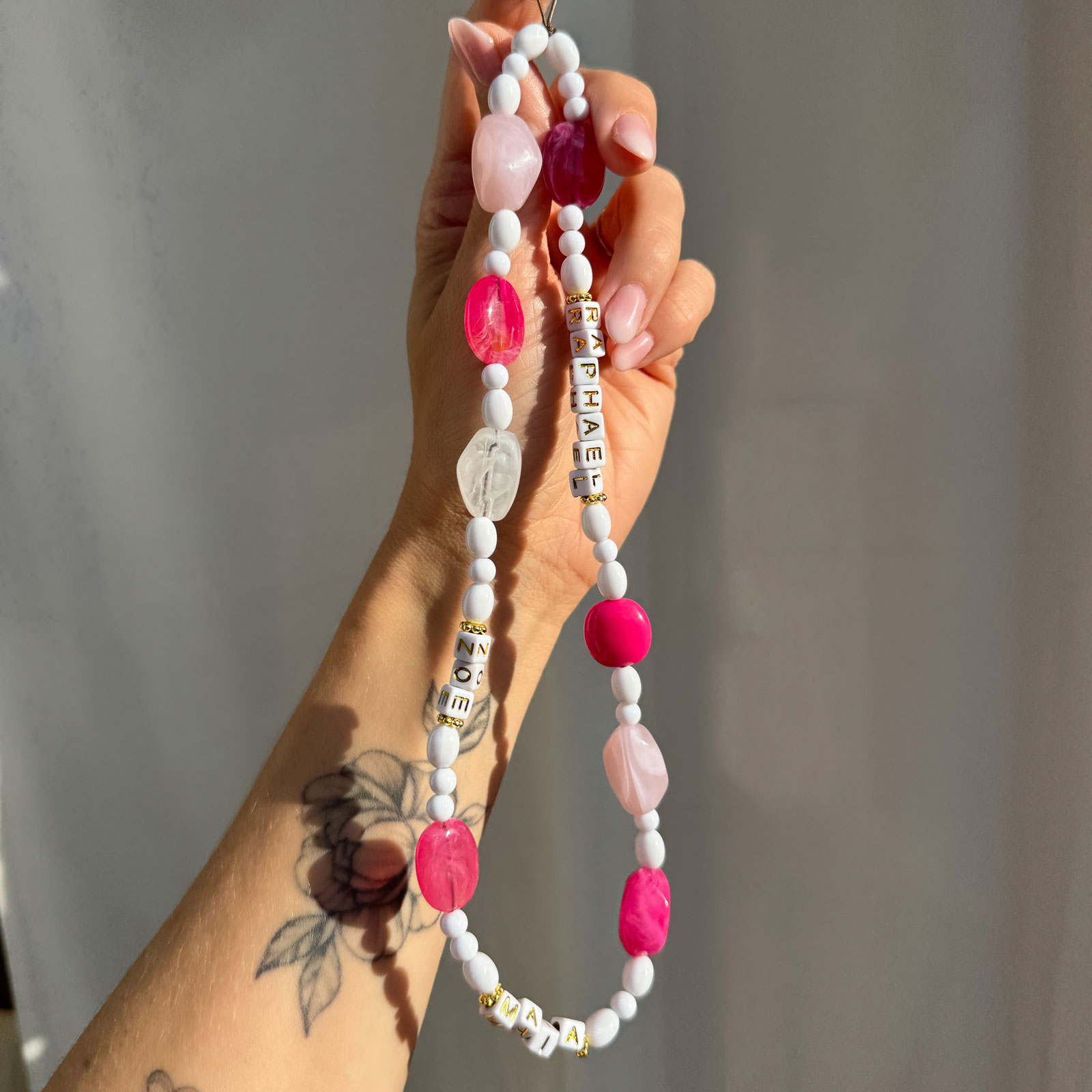 Bracelet de téléphone artisanal personnalisable, en perles blanches, roses et lettres dorées.